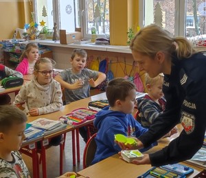 policjantka rozdająca elementy odblaskowe uczniom