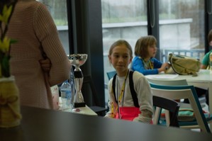 Zdjęcie przedstawia: siedzącą przy stoliku dziewczynkę z pucharem i dyplomem