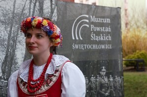 zdjęcie przedstawia: kobietę ubraną w strój ludowy na tle baneru muzeum powstań śląskich w świętochłowicach