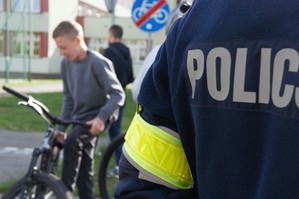 zdjęcie przedstawia: zbliżenie na mundur policjanta, a w tle uczestnik konkursu na rowerze