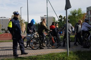 zdjęcie przedstawia: policjanta, a w tle uczestnicy konkursu na rowerze