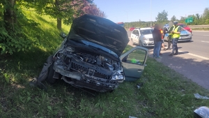 zdjęcie przedstawia: rozbity samochód osobowy a w tle uczestnicy zdarzenia oraz pracujące na miejscu służby