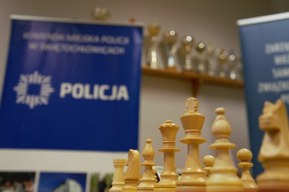 zdjęcie przedstawia: zbliżenie na pionki szachowe a w tle baner z napisem komenda miejska policji w świętochłowicach