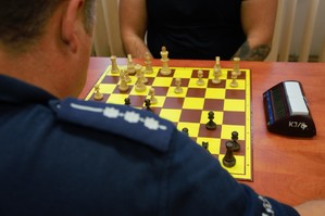 zdjęcie przedstawia: zbliżenie na pagon policyjny a w tle pionki szachowe