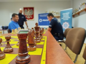 zdjęcie przedstawia: zbliżenie na pionki szachowe a tle policjanci podczas rozgrywki