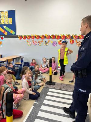 zdjęcie przedstawia policjanta z uczniami szkoły podstawowej omawiającego znaki drogowe