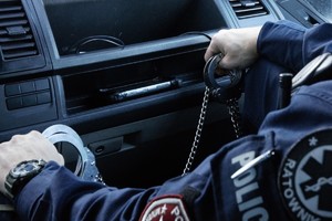 zdjęcie przedstawia policjanta trzymającego kajdanki w ręce