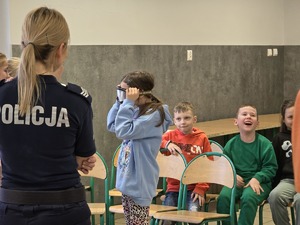 zdjęcie przedstawia policjantkę i dzieci zakładające gogle