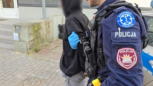 zdjęcie przedstawia policjanta prowadzącego zatrzymanego mężczyznę