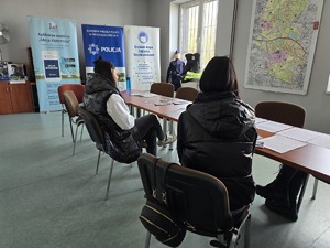 osoby siedzące przy stole rozmawiające z pracownikami policji
