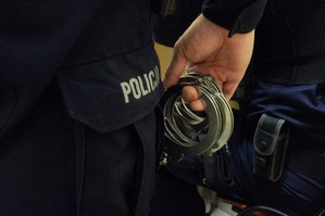 zdjęcie przedstawia policjanta trzymającego kajdanki w ręce