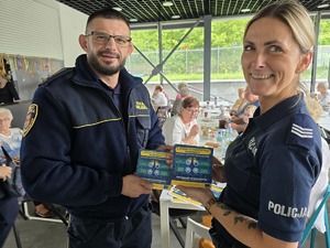 zdjęcie przedstawia policjantkę i strażnika miejskiego trzymającego ulotki