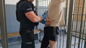 zdjęcie przedstawia policjanta zakładającego kajdanki mężczyźnie