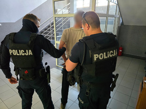 zdjęcie przedstawia policjantów prowadzących zatrzymanego mężczyznę