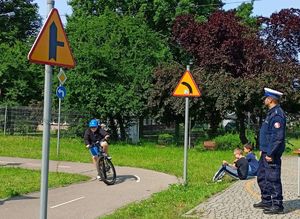 Policjant umundurowany na torze rowerowym, w tle dziecko na rowerze