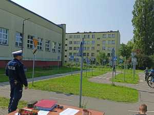 Policjant umundurowany na torze rowerowym, w tle dziecko na rowerze