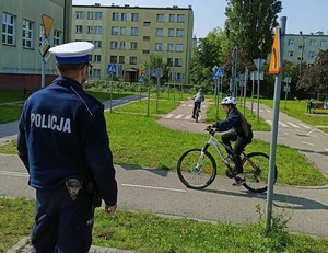 Policjant umundurowany na torze rowerowym, w tle dziecko na rowerze