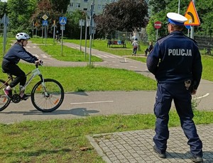 Policjant umundurowany na torze rowerowym, w tle dziecko na rowerze