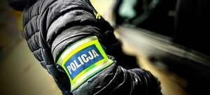 zdjęcie przedstawia nieumundurowanego policjanta z opaską z napisem policja