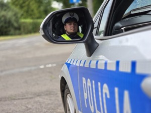 zdjęcie przedstawia odbicie policjanta w lusterku samochodu