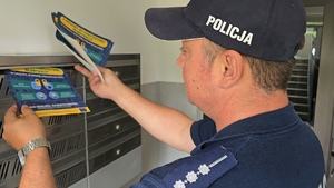 zdjęcie przedstawia policjanta wrzucającego ulotkę do skrzynki na listy
