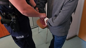 zdjęcie przedstawia policjanta zakładającego kajdanki osobie zatrzymanej