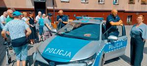 zdjęcie przedstawia dzielnicowego z podopiecznymi domu pomocy społecznej stojących przy radiowozie