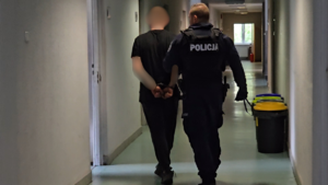 zdjęcie przedstawia policjanta prowadzącego mężczyznę po korytarzu