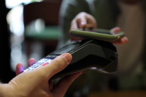 zdjęcie przedstawia jak ktoś przykłada telefon do terminala płatniczego