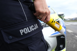 zdjęcie przedstawia policjanta z alkomatem i radiowóz