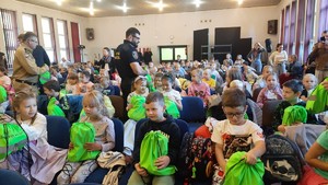 zdjęcie przedstawia: strażaka i strażnika miejskiego wręczających uczniom pleckami odblaskowe