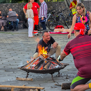 zdjęcie przedstawia mężczyznę piekącego kiełbasę na ognisku