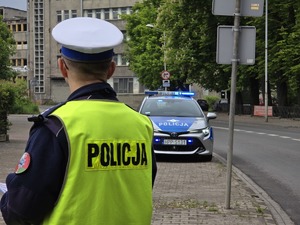 zdjęcie przedstawia policjanta na tle radiowozu
