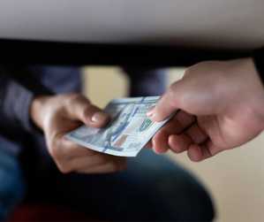 zdjęcie przedstawia osoby wręczające pod stołem pieniądze