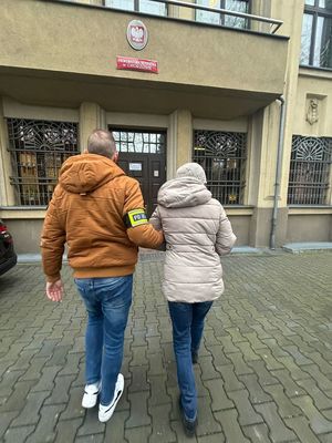 zdjęcie przedstawia nieumundurowanego policjanta prowadzącego zatrzymaną kobietę