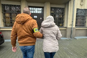 zdjęcie przedstawia nieumundurowanego policjanta prowadzącego zatrzymaną kobietę