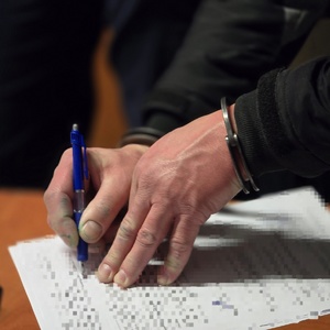 zdjęcie przedstawia mężczyznę w kajdankach podpisującego dokumenty