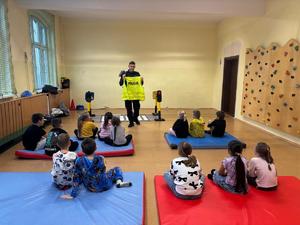 zdjęcie przedstawia policjanta rozmawiającego z dziećmi w szkole