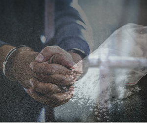 zdjęcie przedstawia mężczyznę w kajdankach i woreczek z białym proszkiem