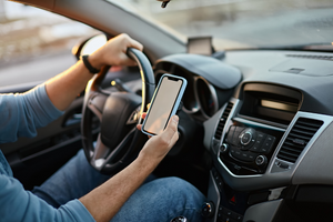 zdjęcie osoby prowadzącej samochód i trzymającej telefon w ręce