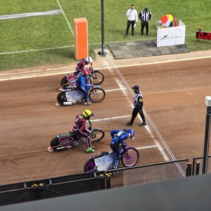 zdjęcie przedstawia zawodników żużlowych podczas wyścigu