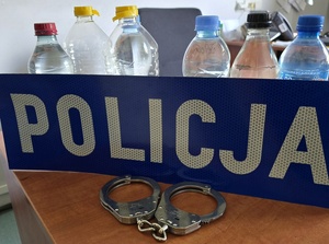 zdjęcie przedstawia napis policja i zabezpieczone butelki z alkoholem