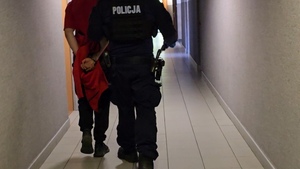zdjęcie przedstawia policjanta prowadzącego zatrzymanego mężczyznę