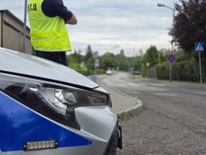 zdjęcie przedstawia zbliżenie na radiowóz a w tle policjanta mierzącego prędkość