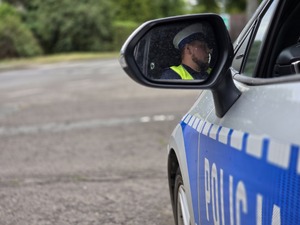 zdjęcie przedstawia odbicie policjanta w lusterku radiowozu