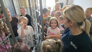 zdjęcie przedstawia policjantkę pokazującą dzieciom policyjną celę