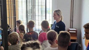 zdjęcie przedstawia policjantkę pokazującą dzieciom policyjną celę