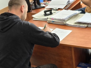 zdjęcie przedstawia zatrzymanego mężczyznę podpisującego dokumenty