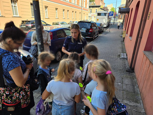 zdjęcie przedstawia policjantkę rozdającą uczniom opaski odblaskowe