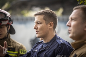 zdjęcie przedstawia policjantów i strażaków stojących przy wraku samochodu i omawiających ćwiczenie